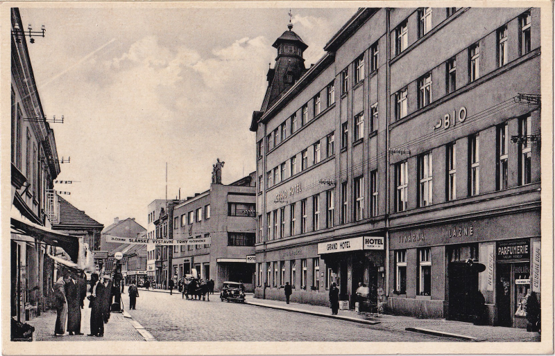 Fotografie pro pohlednici pořízena někdy mezi červnem a červencem 1934, jak informuje transparent. Již jen Grand hotel, s vinárnou, lázněmi a s parfumerií s holírnou a česáním dam.