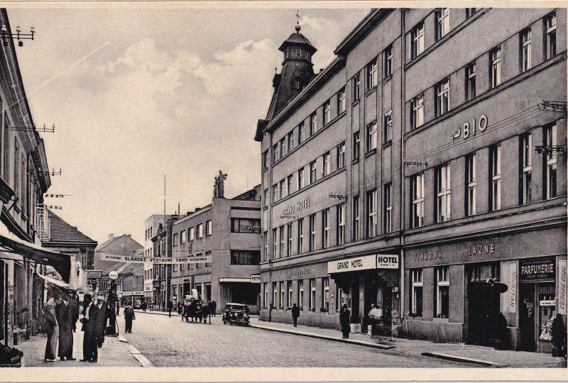 Fotografie pro pohlednici pořízena někdy mezi červnem a červencem 1934, jak informuje transparent. Již jen Grand hotel, s vinárnou, lázněmi a s parfumerií s holírnou a česáním dam.